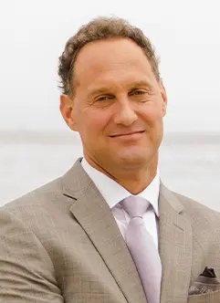 A man in a suit and tie standing next to the ocean.