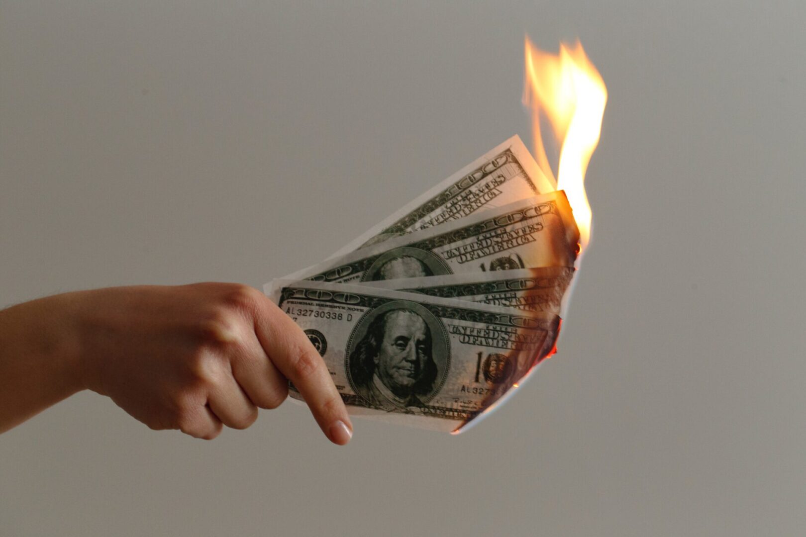 A hand is holding a burning dollar bill.